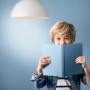Philips LED E14 Tropfenlampe, 6,5W, unter einer weißen Hängelampe liest ein Kind ein blaues Buch.