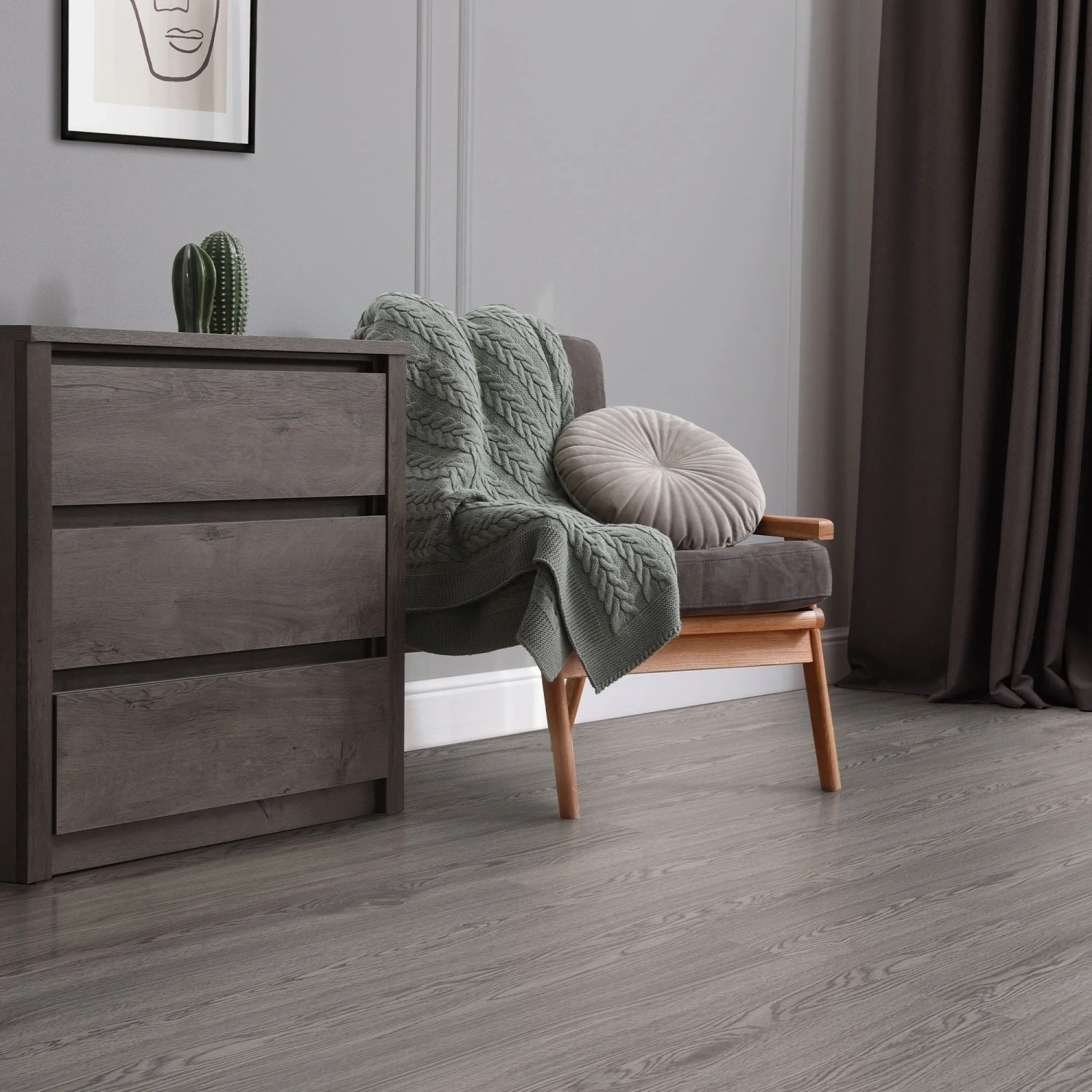 ML-Design Vinylboden Eiche Grau, selbstklebend, als Bodenbelag im Raum mit Kommode und Sessel.