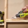 Ryobi Akku-Handsauger RHV18, gelb/schwarz, beim Aufsaugen von Holzspänen, Bohrmaschine im Hintergrund.