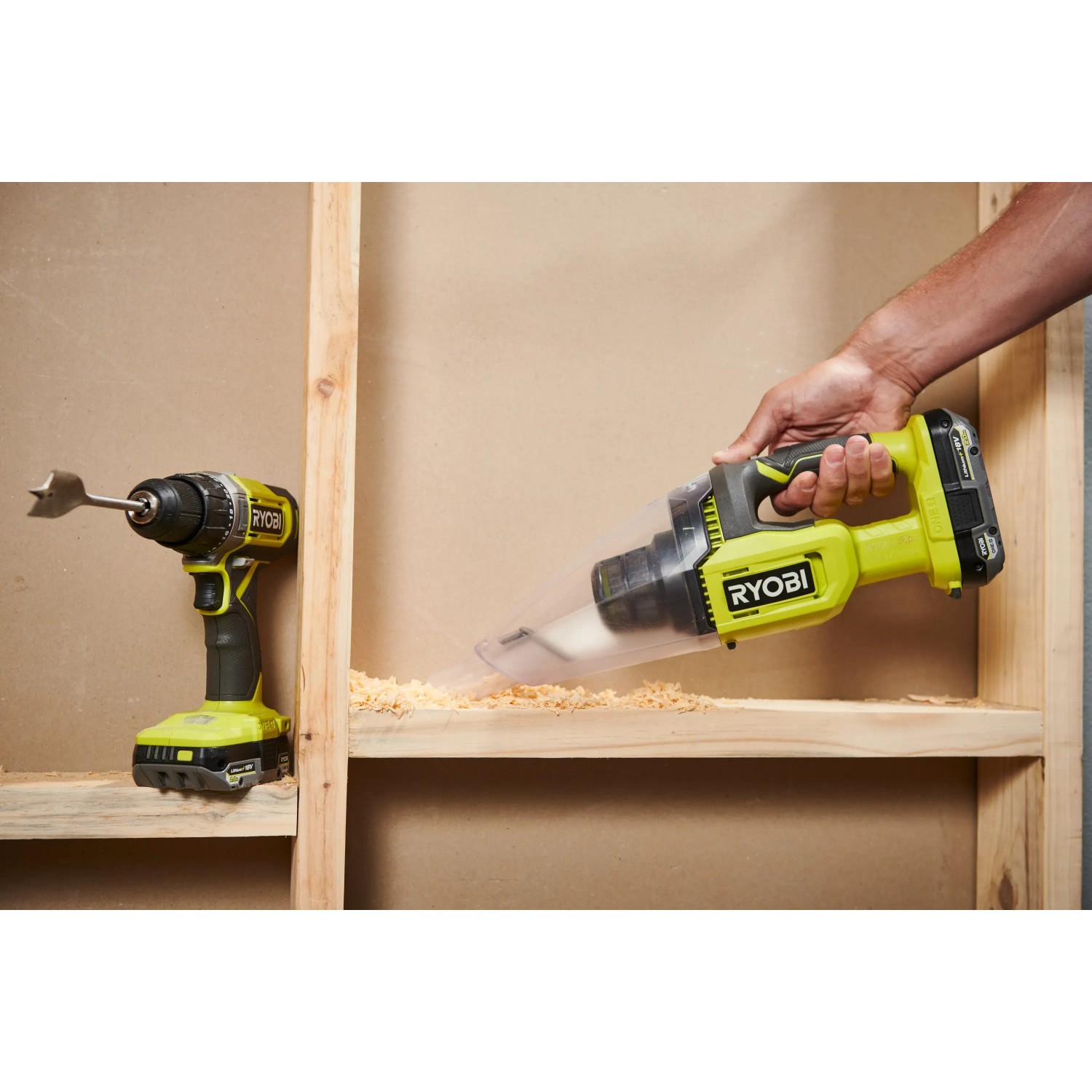 Ryobi Akku-Handsauger RHV18, gelb/schwarz, beim Aufsaugen von Holzspänen, Bohrmaschine im Hintergrund.
