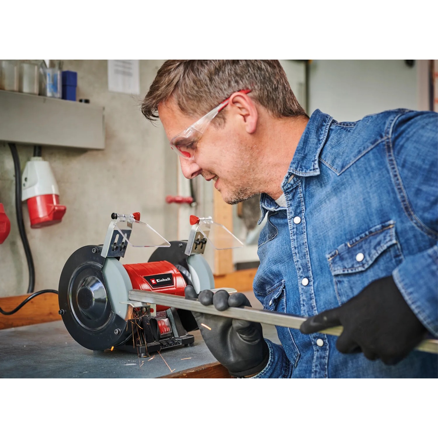 Mann schleift Metall mit Einhell Doppelschleifer TC-BG 150. Schleifmaschine mit Funkenschutz.