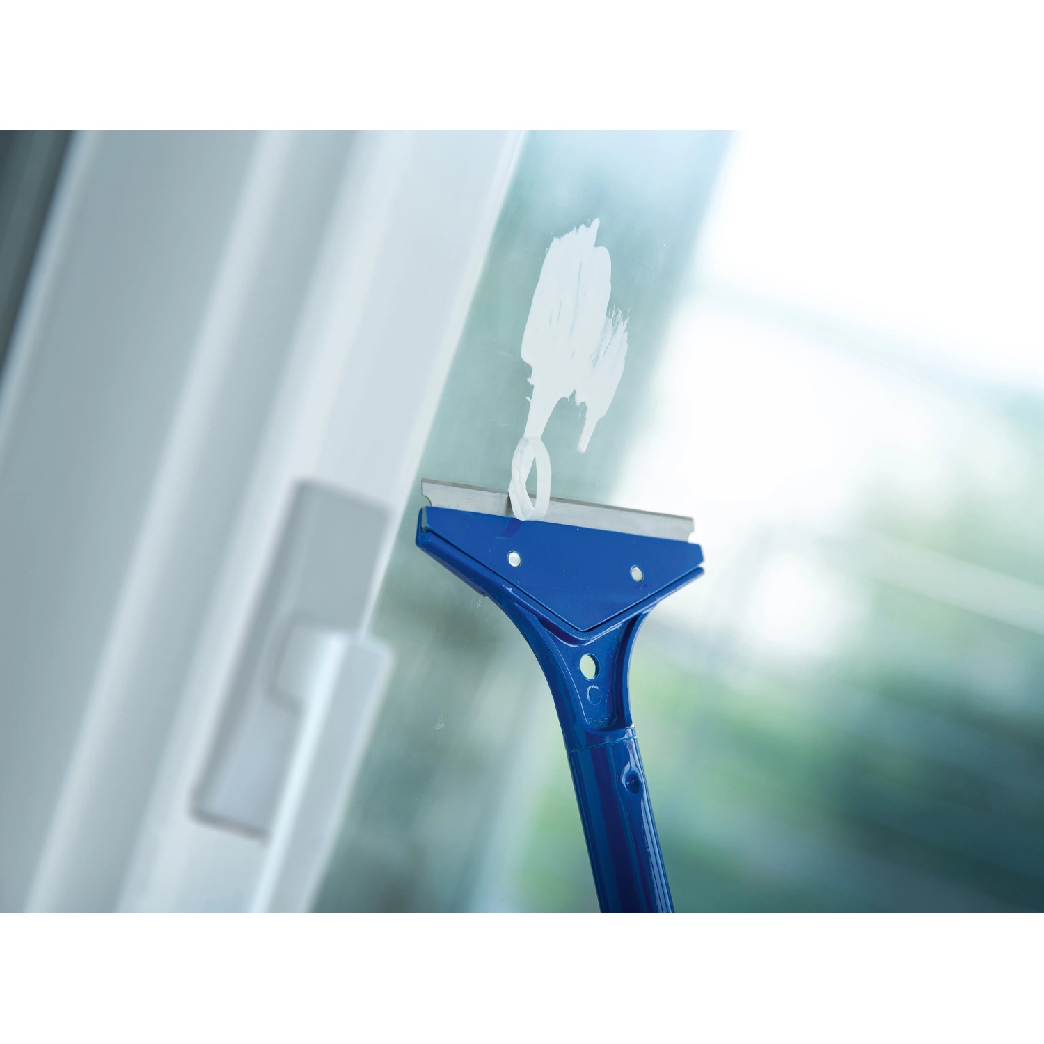 LUX Fenster- und Bodenschaber im Einsatz zum Entfernen von Farbresten auf einer Fensterscheibe.