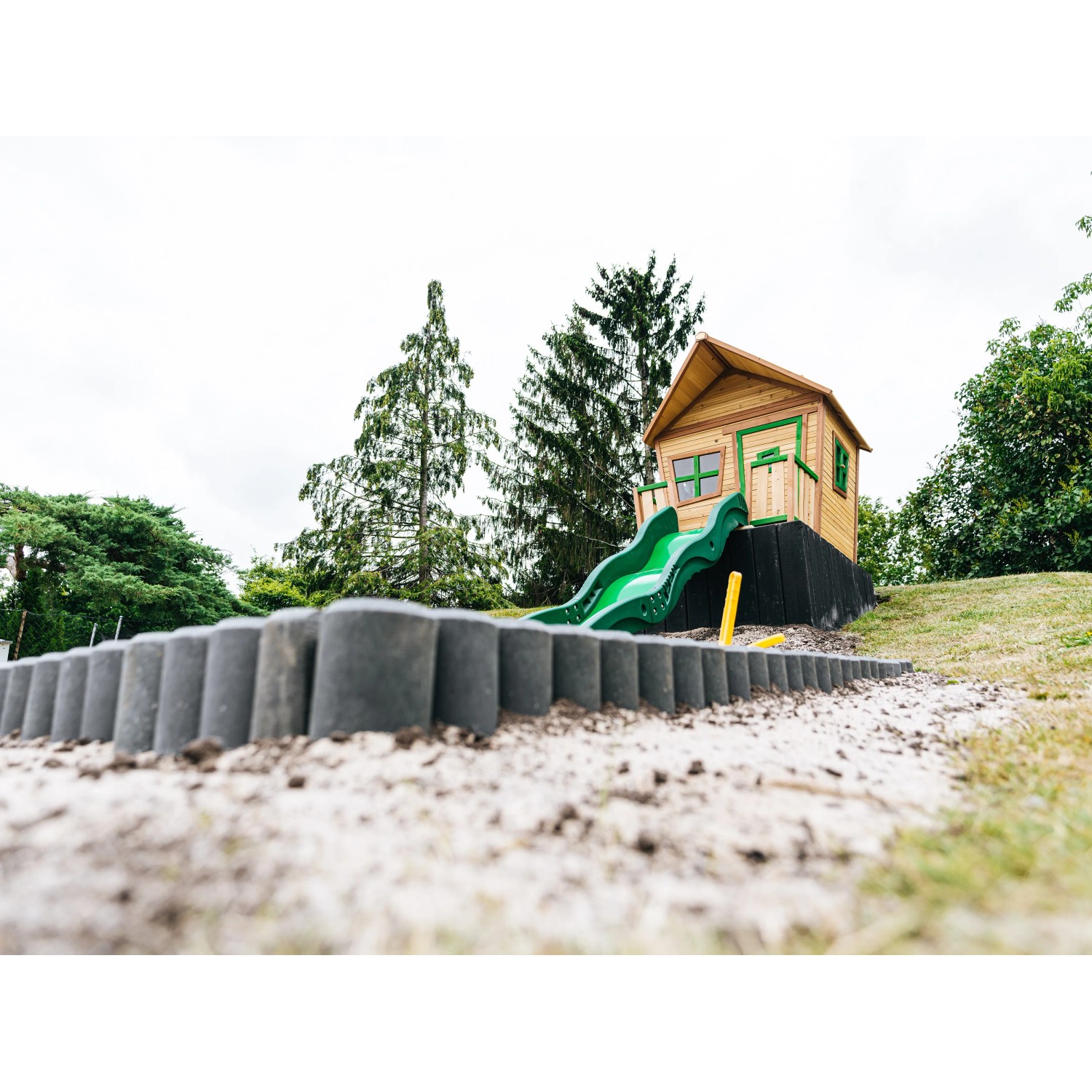 Axi Spielhaus Max mit Rutsche, Leiter und Sandkasten in Braun/Grün. Spielturm im Comic-Stil für Kinder.