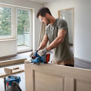 Mann hobelt eine Holztür mit dem blauen Bosch Akku-Hobel GHO 18V-26. Ideal für glatte Oberflächen und präzise Holzarbeiten.