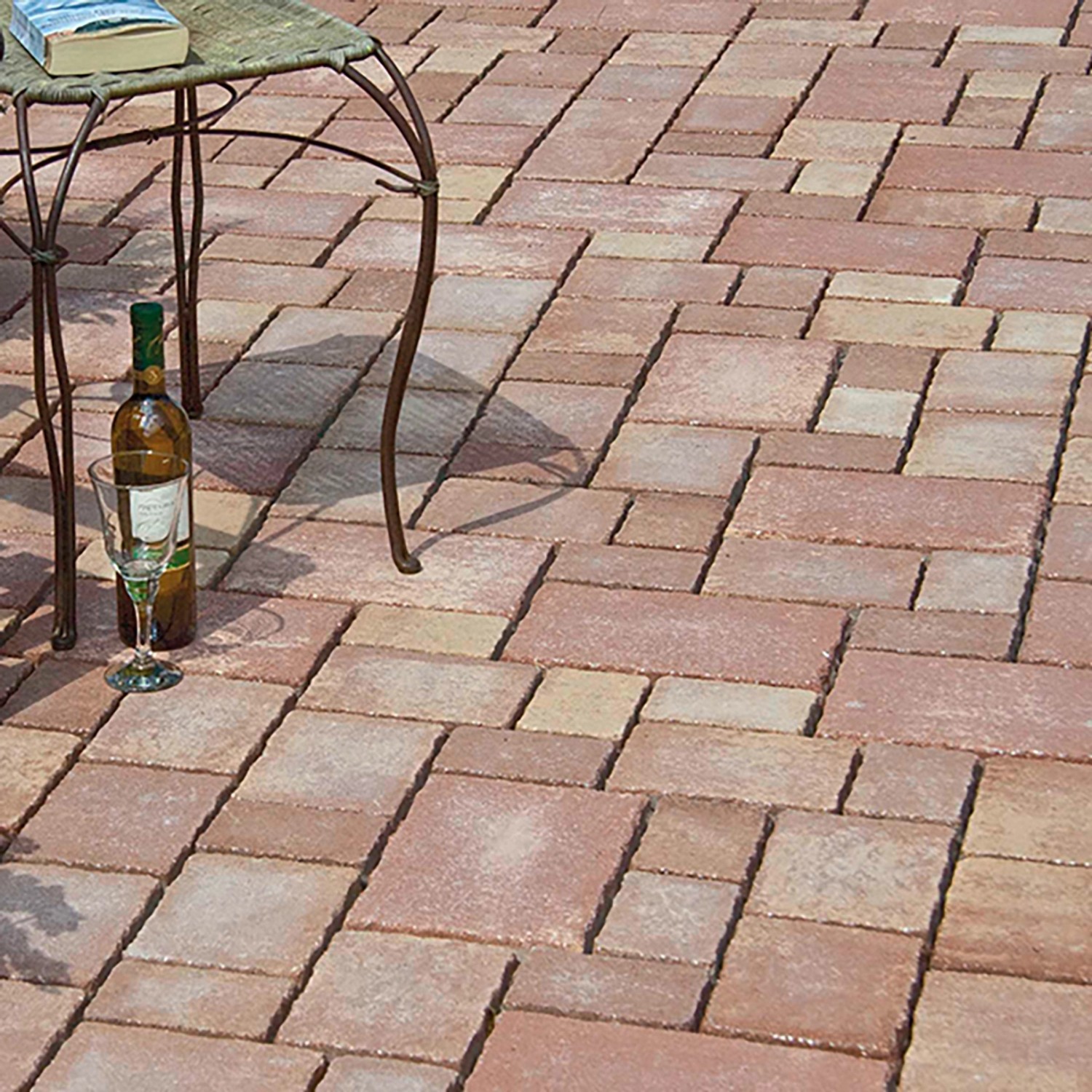 Verlegte Mehrformat-Pflastersteine Encanto Beton Antik Terra-Nuanciert mit Tisch, Wein und Buch im Garten.