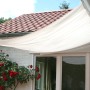 Weißes Peddy Shield Sonnensegel (330x200 cm) am Haus montiert. Ideal für Terrasse und Garten.