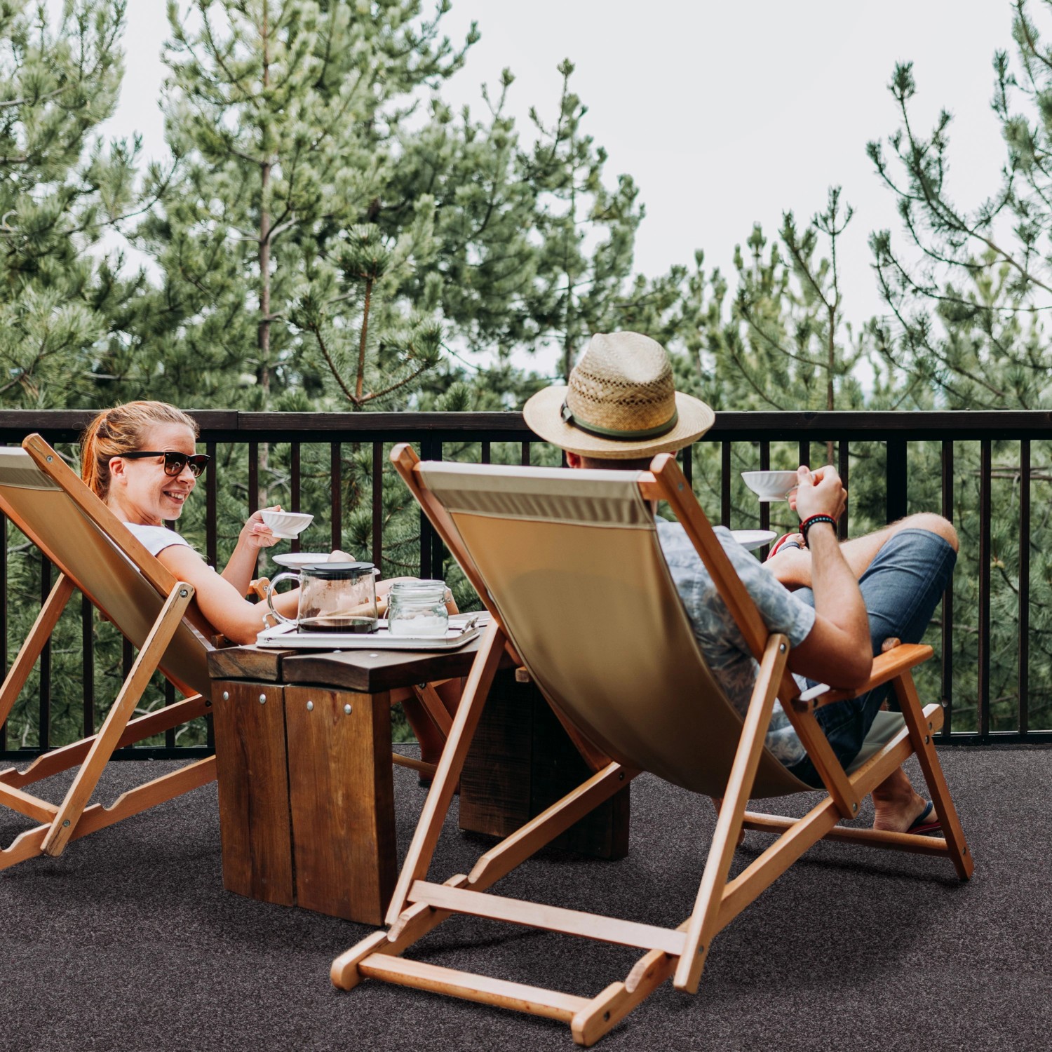Szene mit Primaflor Rasenteppich Green Braun: Paar entspannt auf Balkon mit Kunstrasen.
