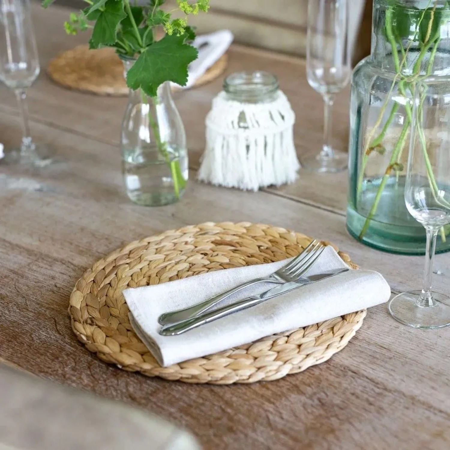 Rundes, geflochtenes Tischset aus Wasserhyazinthe mit Besteck und Serviette auf rustikalem Holztisch. 30 cm Platzset.