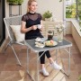 Grauer WOLTU Campingtisch Klapptisch aus Aluminium, zusammengeklappt mit Frau auf Balkon.
