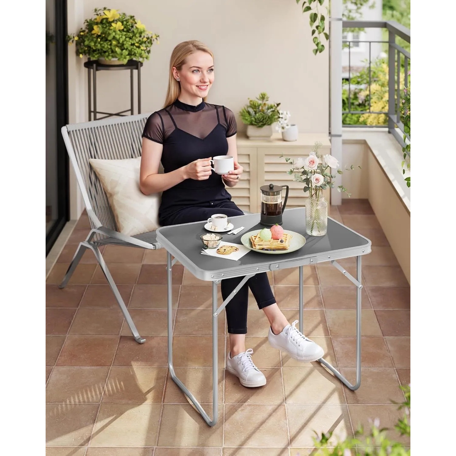 Grauer WOLTU Campingtisch Klapptisch aus Aluminium, zusammengeklappt mit Frau auf Balkon.