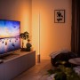 Weiße Philips Hue Gradient Signe Stehleuchte im Wohnzimmer mit Farbverlauf an der Wand.