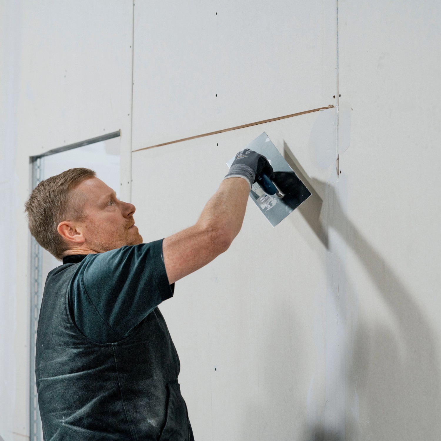 Handwerker verspachtelt Gipskartonplatte (9,5mm) an Wand. Trockenbau im Innenbereich.