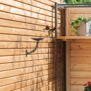 Braune Gusseisen Vogeltränke mit Blumendesign an Holzwand, Spatz fliegt an. Ideal für Garten, Balkon.