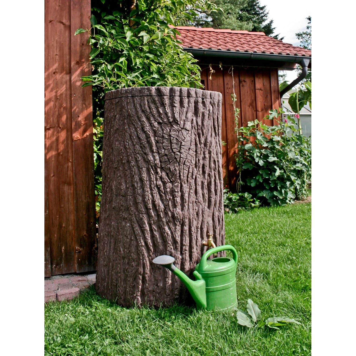 Arves Regentonne Evergreen 475 l in Dunkelbraun mit Baumstammoptik und grüner Gießkanne im Garten.