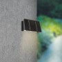 Schwarze LED Solar-Wandleuchte Cariati (17x11x6,5cm) an grauer Wand. Solar-Wandlampe für Aussen.