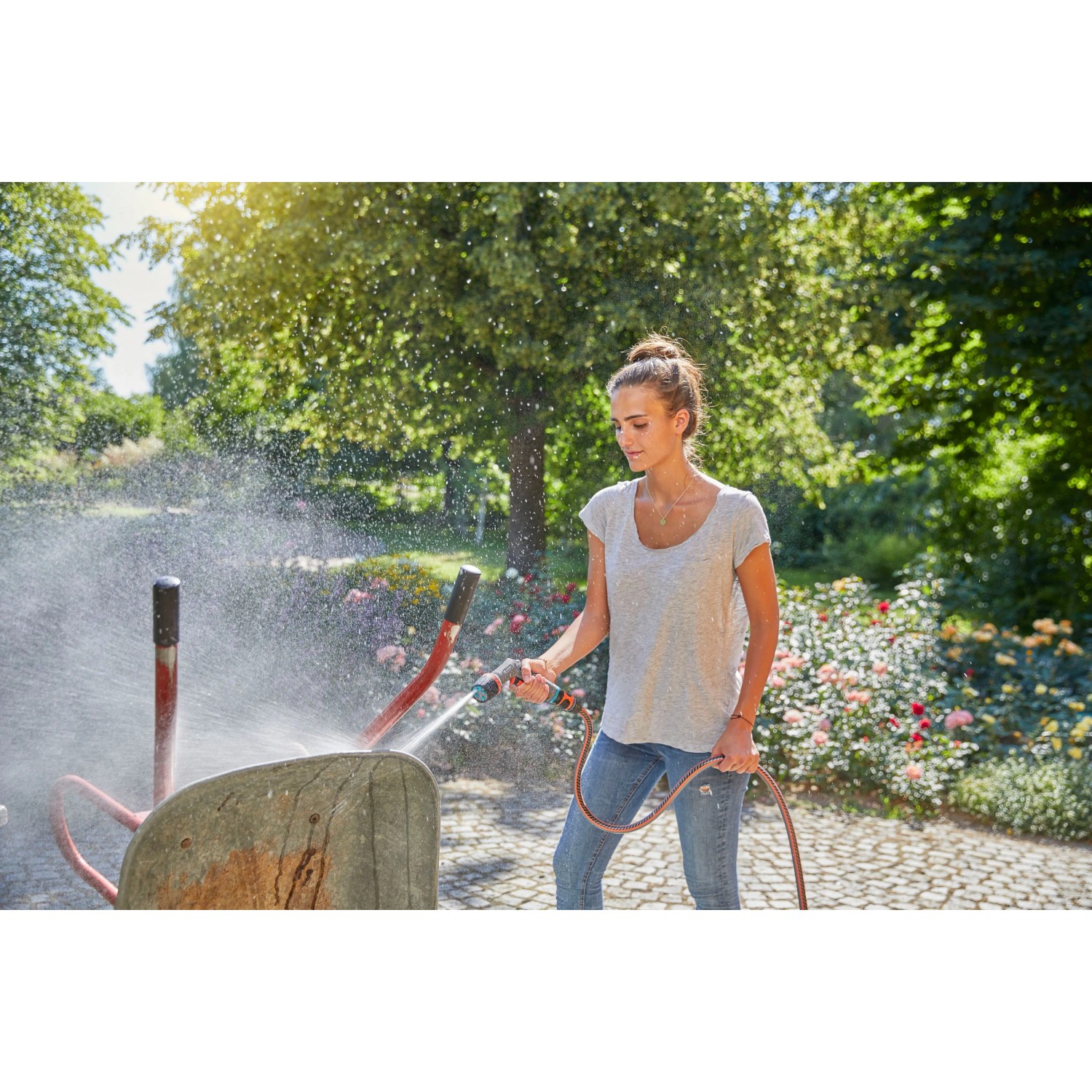 Frau reinigt Schubkarre mit Gardena Comfort Reinigungsspritze ecoPulse™ im Garten.
