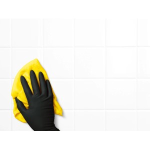 Hand mit schwarzem Einmalhandschuh reinigt Fliesen mit gelbem Tuch.