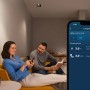 Paar steuert Bosch Smart Home Licht-/Rollladensteuerung per App im Wohnzimmer, zeigt Energieverbrauch.