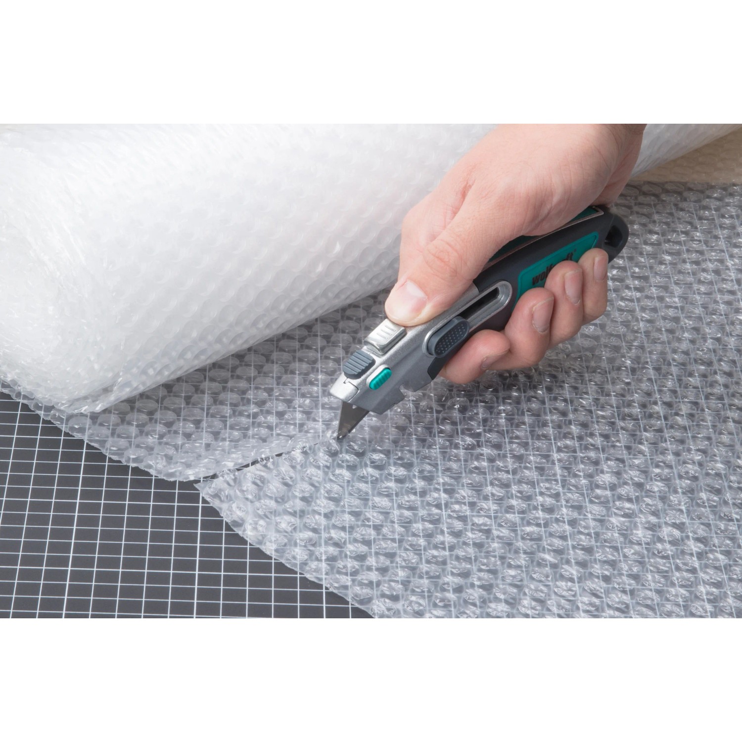 Hand schneidet Luftpolsterfolie mit wolfcraft Profi-Dual-Sicherheitsmesser. Messer mit Trapezklinge.