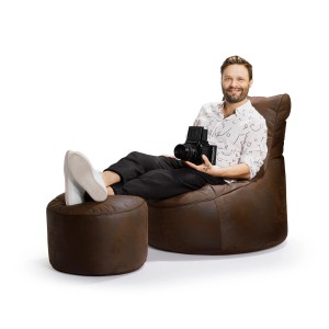 Mann entspannt im braunen Sitting Point Sessel Cuba mit Hocker und Kamera.