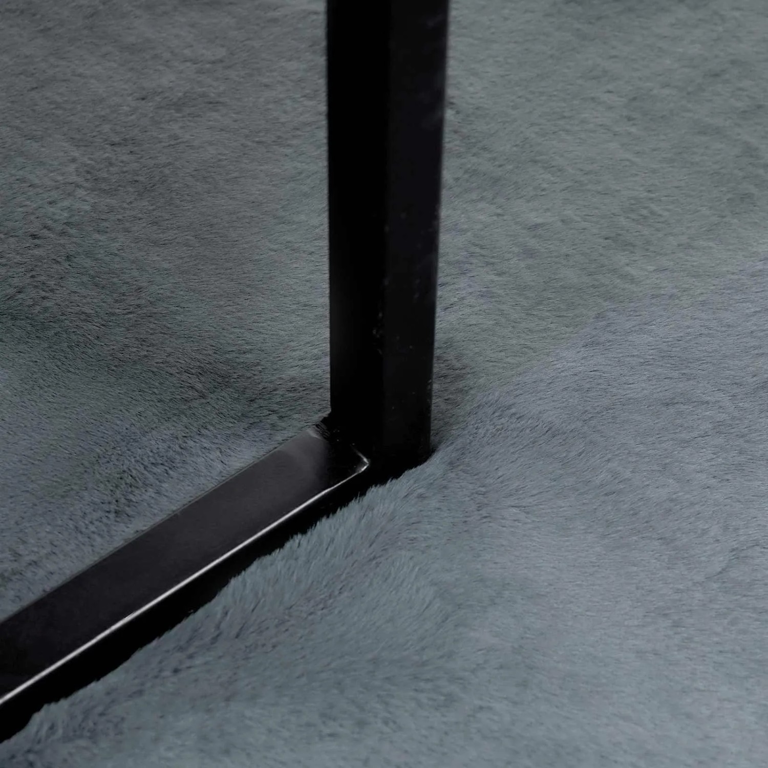 Nahaufnahme eines anthrazitfarbenen Kunstfellteppichs mit plüschiger Oberfläche und schwarzem Metallbein. Extra weich, modern.