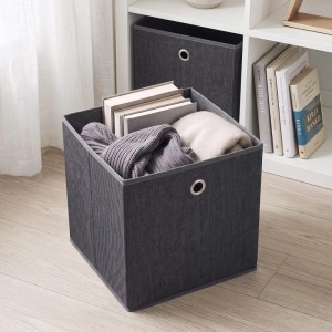 Dunkelgraue faltbare Stoffbox (33x33x33 cm) mit Metallöse, gefüllt mit Büchern und Kleidung, im Regal. Für Aufbewahrung.