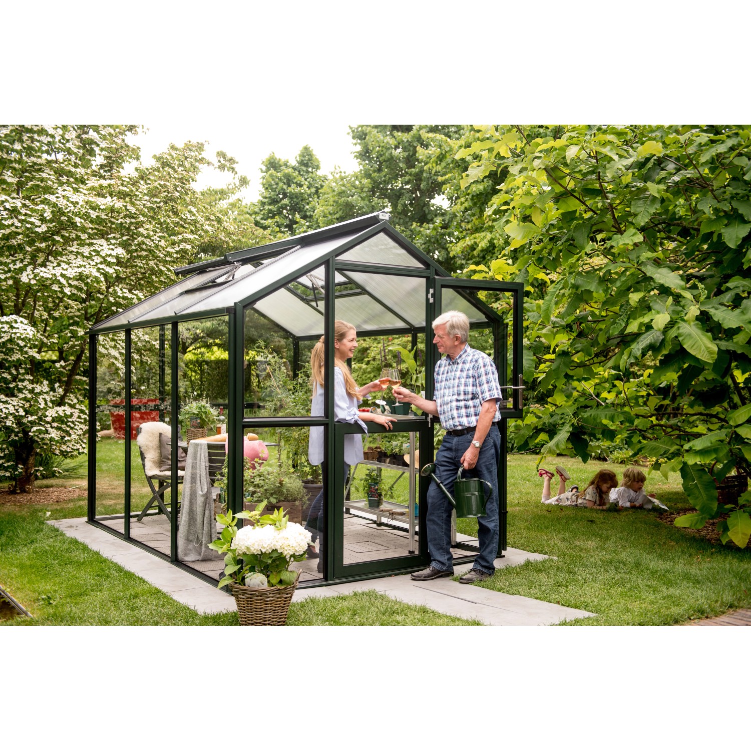 KGT Gewächshaus Galant III, tannengrün, mit Personen im Garten. Ideal für Pflanzenzucht.