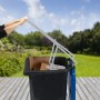 Graue Relaxdays Müllpresse aus Stahl in Gebrauch, eine Person presst Müll in schwarzer Tonne im Garten.
