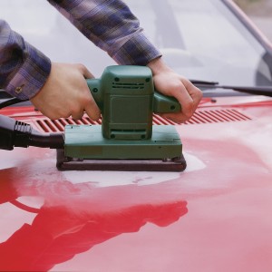 Schwingschleifer mit LUX Schleifvlies-Set im Einsatz auf roter Oberfläche.