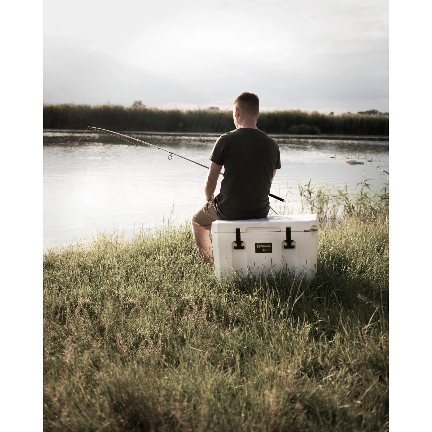 Petromax Kühlbox Sand 50L: Angler sitzt auf der Box am See.
