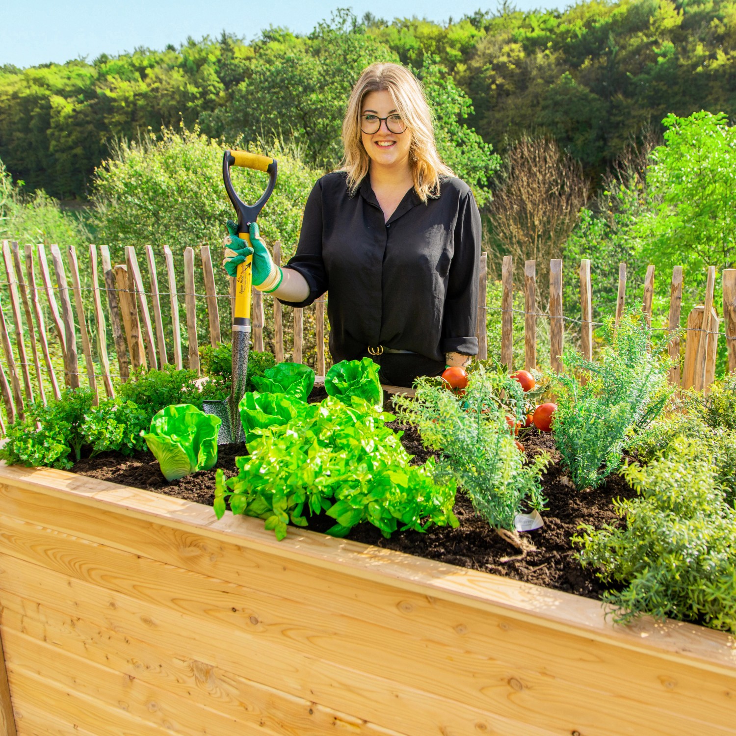 Westmann Hochbeet aus Lärche mit Bepflanzung und Frau mit Spaten im Garten.
