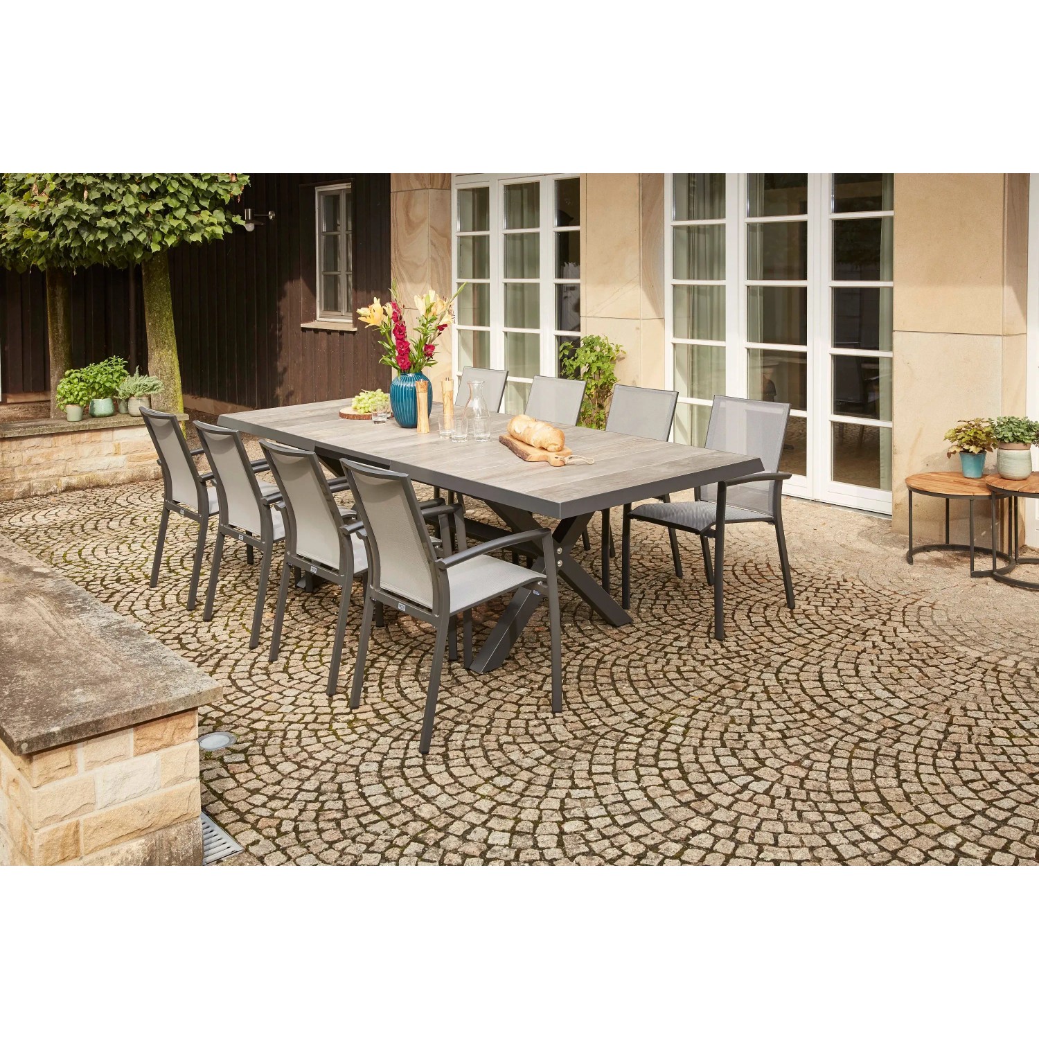 Anthrazitfarbener Siena Garden Stapelsessel Velia aus Aluminium, 56x66x89 cm, mit Gartentisch und weiteren Gartenstühlen.