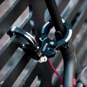 Master Lock Street Cuff 8200EURDPRO Schellenschloss in Schwarz-Silber sichert ein Fahrrad an einem Zaun.