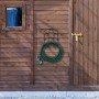 Schwarzer Stahl Schlauchhalter an Holzwand mit grünem Gartenschlauch und Spritze. Platzsparende Wandmontage.