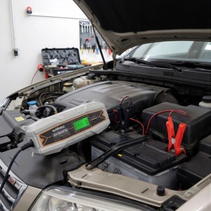 Wiltec Batterieladegerät 6-12V mit LCD-Display lädt eine Autobatterie im Motorraum. Kfz-Ladegerät für Autoelektrik.