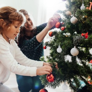 Kind und Erwachsener schmücken einen Christbaum mit glänzenden, matten und glitzernden Weihnachtskugeln aus Kunststoff.