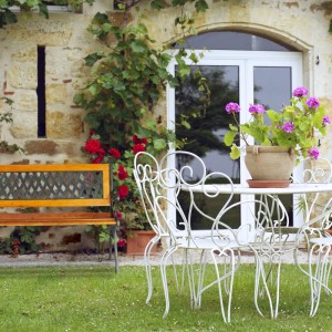 Braune Relaxdays Gartenbank aus Holz und Gusseisen, mit dekorativer Rückenlehne, als Zweisitzer im grünen Garten.