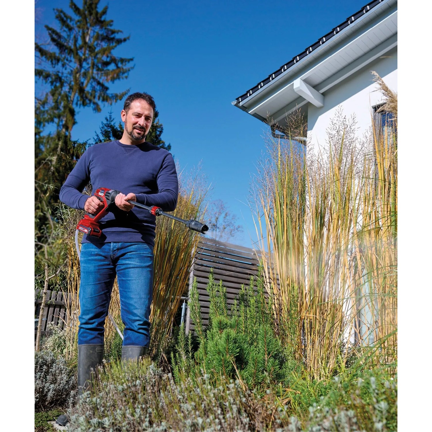 Mann reinigt Garten mit Einhell Akku-Druckreinigerpistole Hypresso. Kabelloses Reinigungsgerät für Haus & Garten.