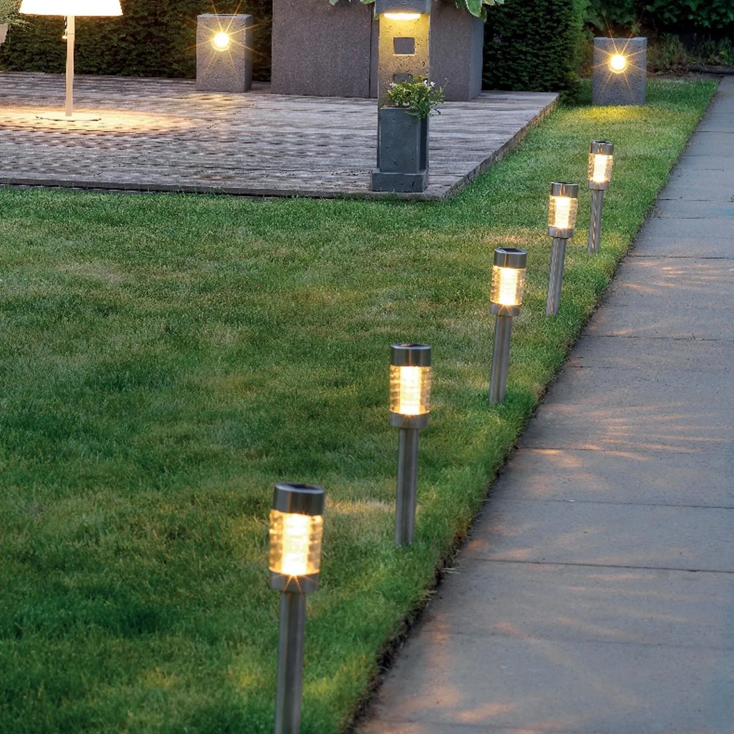 Zehn Marelida LED Solar Wegleuchten aus Edelstahl mit Erdspieß säumen einen Gartenweg. Sie spenden warmweißes Licht und sind 15cm hoch.