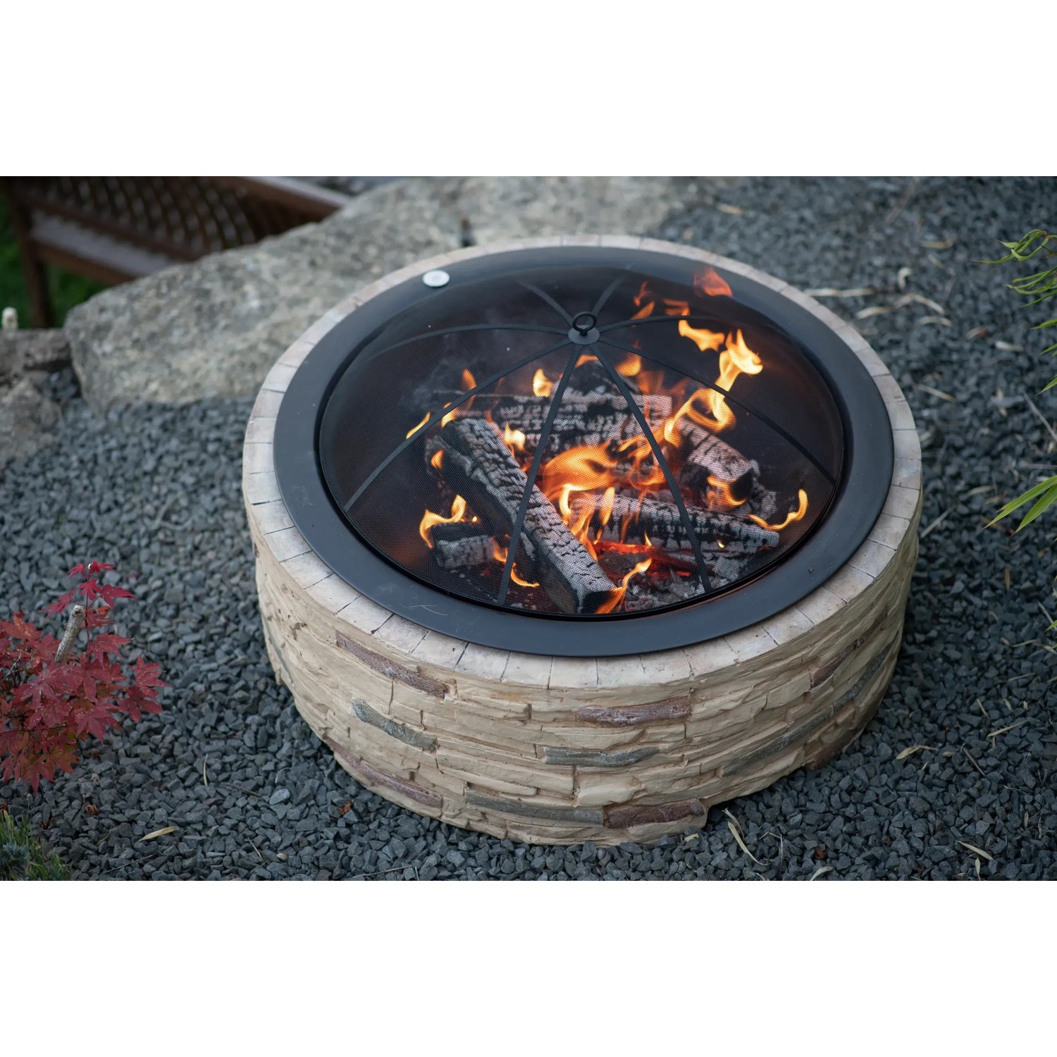 Westmann Feuerstelle in Steinoptik mit Funkenschutzgitter und brennendem Holz.