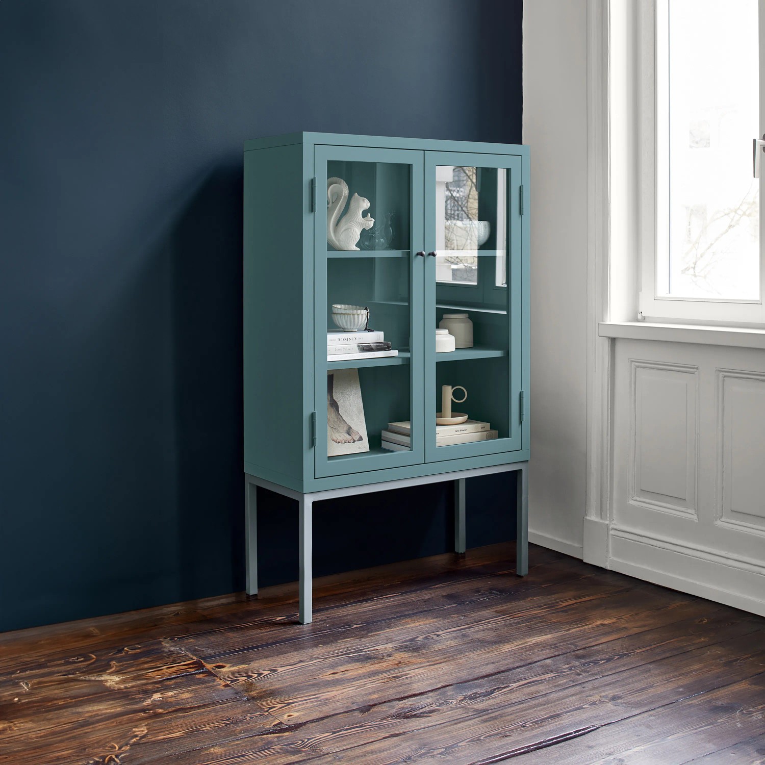 Blauer Buntlack-Schrank „Quelle der Gelehrten“ von Alpina Feine Farben mit Glasfront und Deko.