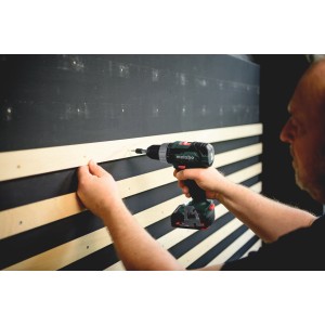 Metabo Akku-Bohrschrauber BS 18 L beim Schrauben in Holzleiste vor schwarzer Wand.