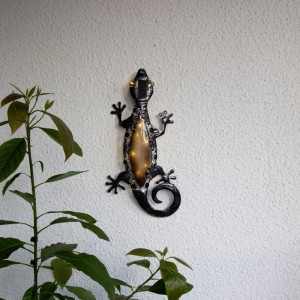 Schwarze LED-Solar-Wanddeko in Geckoform mit warmweissen Lichtern, an heller Wand montiert. Für Garten & Balkon.