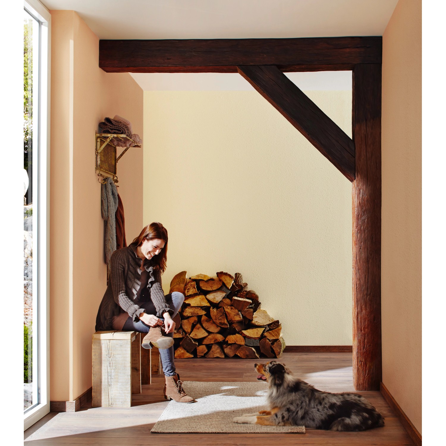 Frau bindet Schuh in terracottafarbenem Raum, gestaltet mit Knauf Compact Color. Holzstapel und Hund im Bild.