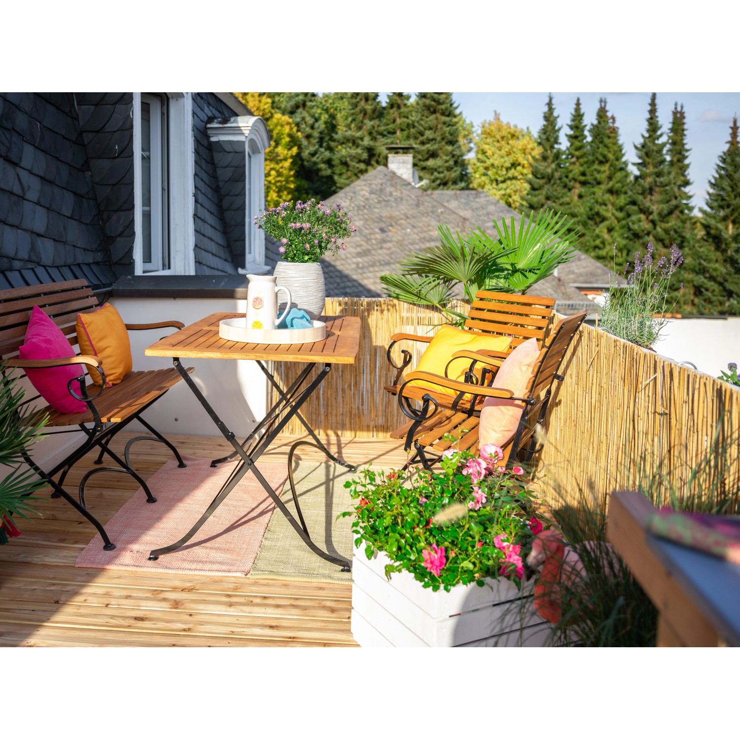 Balkon mit Schilfrohrmatte als Sichtschutz, Gartenmöbeln und Pflanzen.