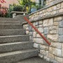 Brauner Aluminium-Handlauf in Eiche-Optik mit silbernen Edelstahl-Halterungen an Steintreppe im Außenbereich. Sicherer Halt.