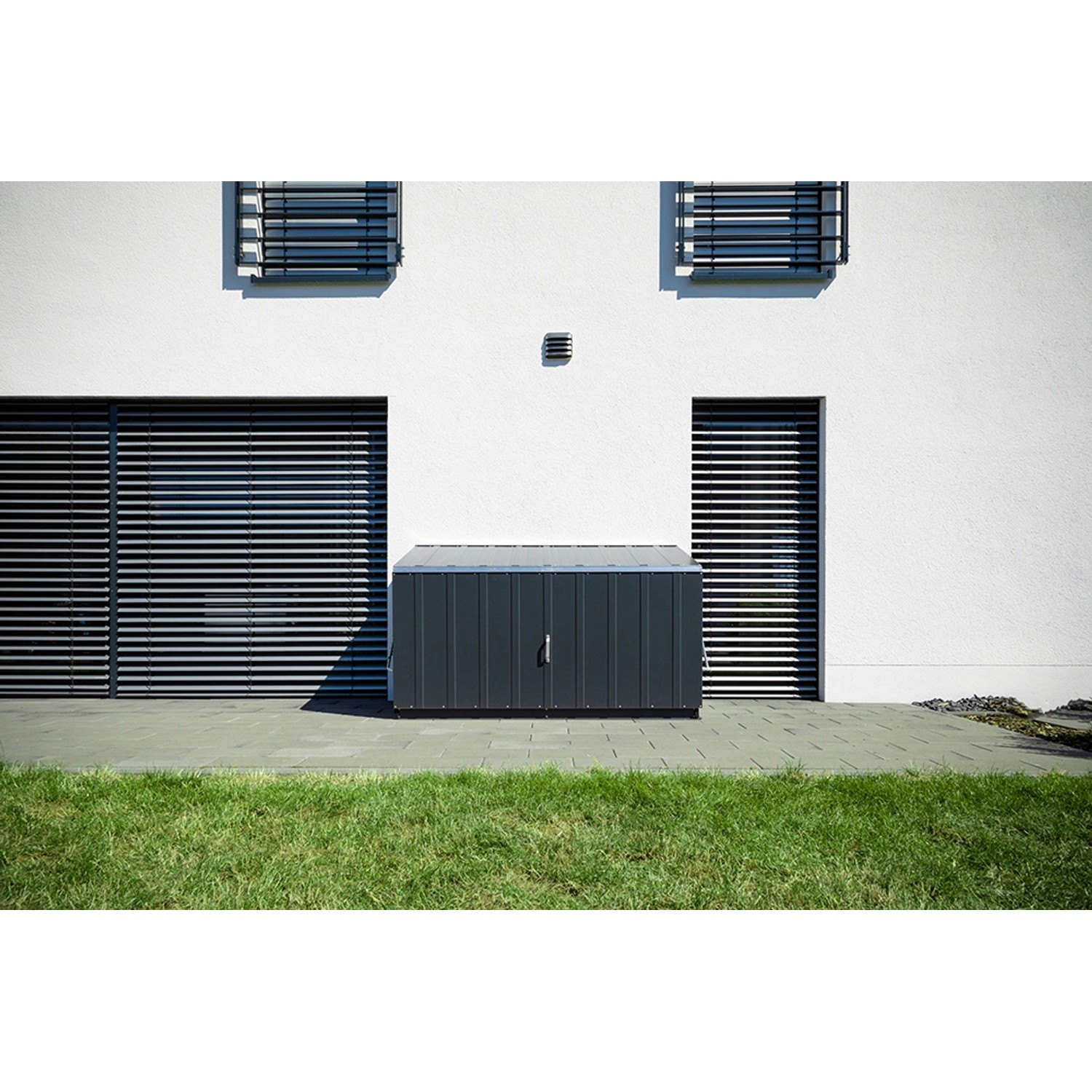 Anthrazitfarbene Trimetals Aufbewahrungsbox Storeguard (196x89cm) vor weißer Hauswand.