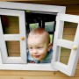 Kind schaut aus Fenster vom braun-weißen Axi Robin Spielhaus mit grauer Rutsche.