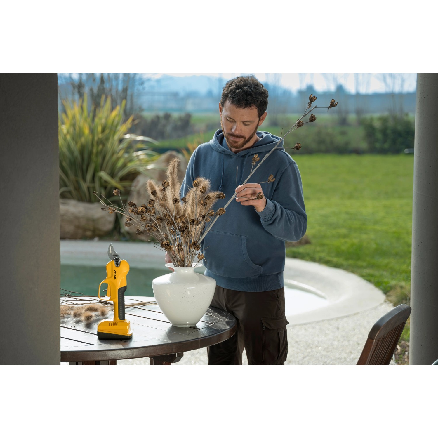 Stiga Akku-Astschere SC 100er mit Mann im Garten, schneidet Äste für eine Vase.