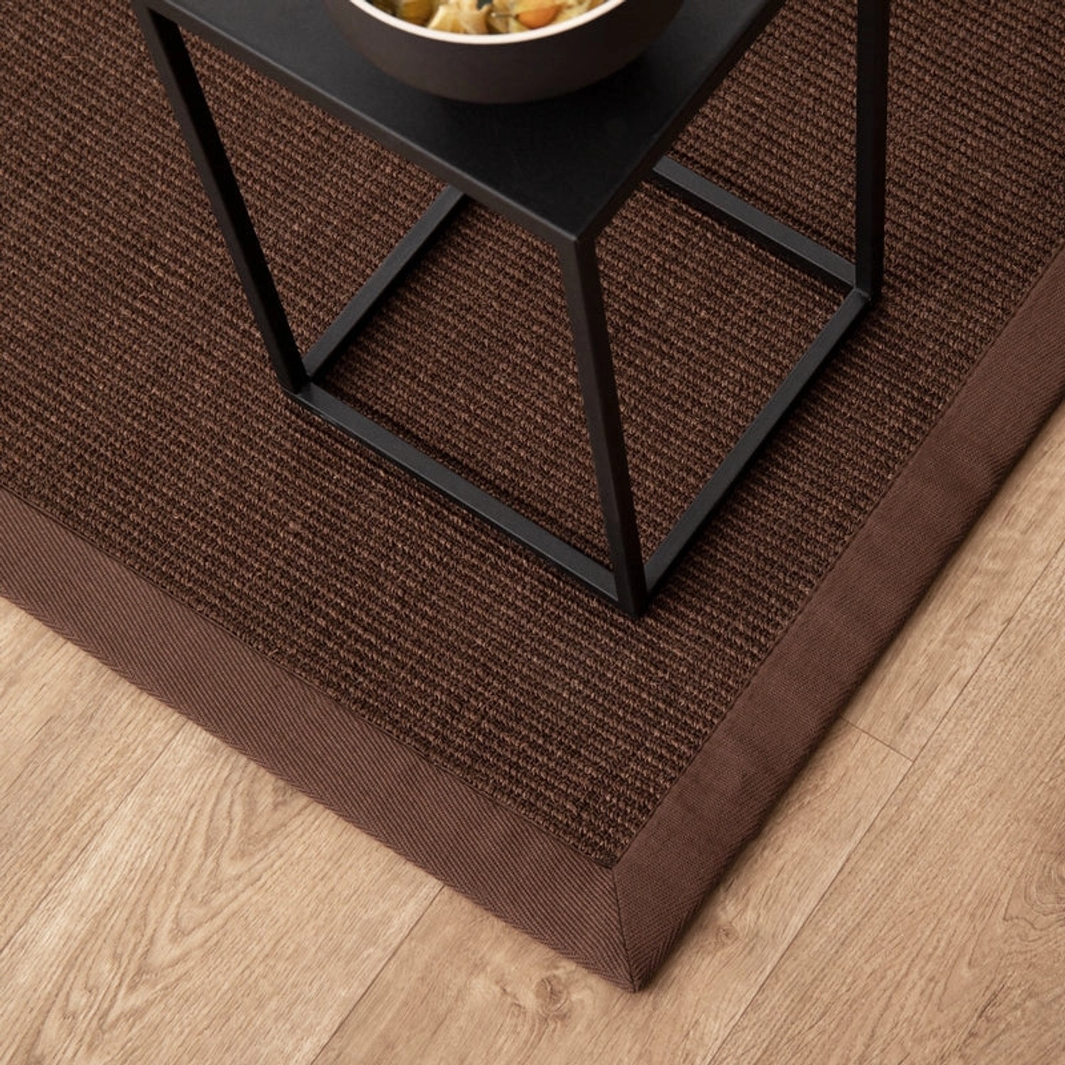 Dunkelbrauner Sisalteppich Amazonas mit breiter Bordüre, 70x130 cm, im Wohnbereich.